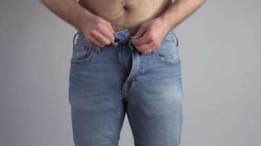 Şişman ve şişman bir adam kotun fermuarını iliklemeye çalışıyor. Şişman adam pantolon giymeye çalışıyor.