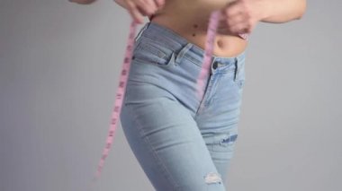 Mavi kotlu zayıf kadın kilo verdikten sonra belini ölçüyor. Kadın kilo verdiğini gösteriyor..