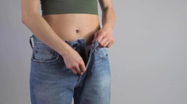 İnce kadın fermuarını büyük beden kot pantolona iliştiriyor ve kilo verdikten sonra belinin mükemmel olduğunu gösteriyor..