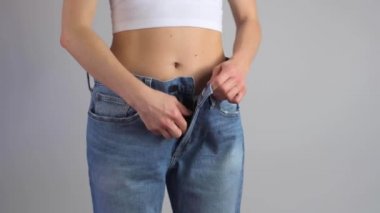 İnce kadın fermuarını büyük beden kot pantolona iliştiriyor ve kilo verdikten sonra belinin mükemmel olduğunu gösteriyor..