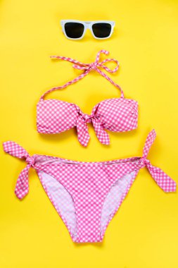 İki yüzme adet pembe etmek takım elbise ve sarı arka plan üzerinde beyaz güneş gözlüğü üstten görünüm.