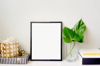 Siyah fotoğraf çerçevesi, yeşil bitki kristal vazo, hediye kutuları ve bir yığın kitap emty gri duvara düzenlenmiştir. Çerçeve mock-up.