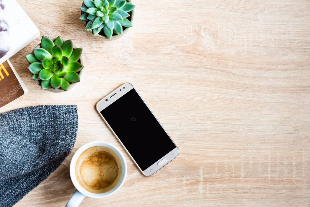 Top view of cosy home scene. Books, woolen blanket, cup of coffee, phone and succulent plants over wooden background. Copy space, mock-up.