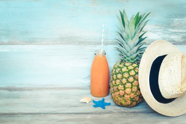 Yaz konsepti stillife - olgun ananas, hasır şapka ve mavi rustik ahşap arka plan önünde multivitamin suyu bir şişe.