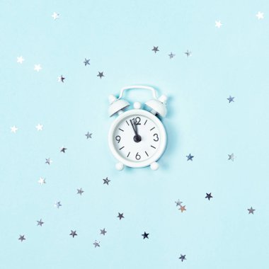 Beyaz klasik çalar saat, gümüş yıldız pullu mavi arka plan üzerinde gece yarısına beş dakika kaldığını gösteriyor. Yeni Yıl Gelişi.