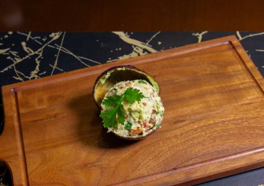 Avokado kabuğuna yerleştirilmiş guacamole, sarı bir arka plana karşı ahşap bir tahta üzerine yerleştirilmiş.
