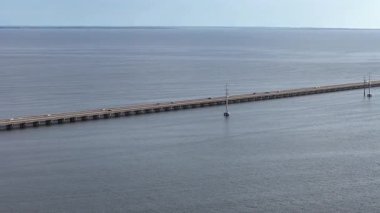 Kill Devil Hills ve Point Harbor arasında sakin bir denizi geçerek uzak ufka doğru düz bir Wright Memorial köprüsünün havadan görüntüsü. Güneş suda parlıyor, huzur verici bir sahne yaratıyor..