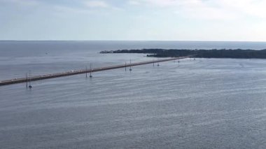 Kill Devil Hills ve Point Harbor arasında sakin bir denizi geçerek uzak ufka doğru düz bir Wright Memorial köprüsünün havadan görüntüsü. Güneş suda parlıyor, huzur verici bir sahne yaratıyor..