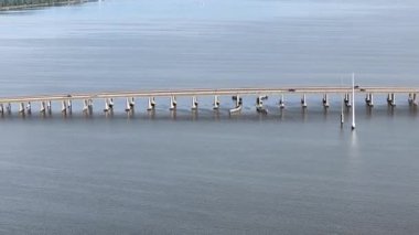 Kill Devil Hills ve Point Harbor arasında sakin bir denizi geçerek uzak ufka doğru düz bir Wright Memorial köprüsünün havadan görüntüsü. Güneş suda parlıyor, huzur verici bir sahne yaratıyor..