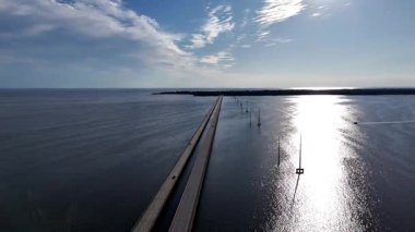 Kill Devil Hills ve Point Harbor arasında sakin bir denizi geçerek uzak ufka doğru düz bir Wright Memorial köprüsünün havadan görüntüsü. Güneş suda parlıyor, huzur verici bir sahne yaratıyor..
