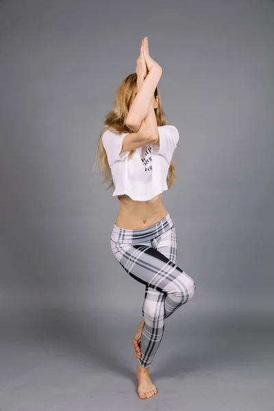 Deportiva hermosa joven practicando yoga, ejercitándose vistiendo ropa deportiva gris y blanca, estudio, larga duración — Foto de Stock