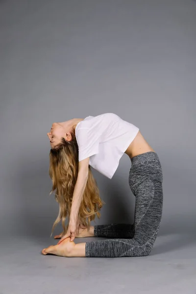 Desportivo bela jovem praticando ioga, trabalhando fora vestindo roupas esportivas cinza e branco, estúdio, comprimento total — Fotografia de Stock