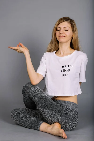 Desportivo bela jovem praticando ioga, trabalhando fora vestindo roupas esportivas cinza e branco, estúdio, comprimento total — Fotografia de Stock