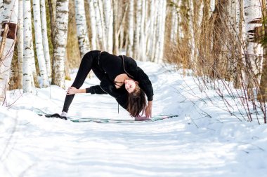 Karda yoga. Parkta yoga yapan bir kız. Yılın kış zamanı. Karla kaplı ağaçlar.