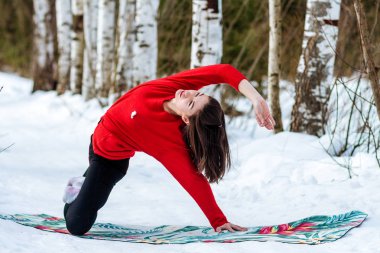 Karda yoga. Parkta yoga yapan bir kız. Yılın kış zamanı. Karla kaplı ağaçlar.