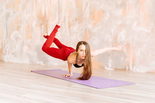 Menina Yoga em cima preto e leggings vermelhos está em uma mão no esteira — Fotografia de Stock