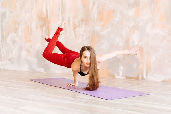 Menina Yoga em cima preto e leggings vermelhos está em uma mão no esteira — Fotografia de Stock