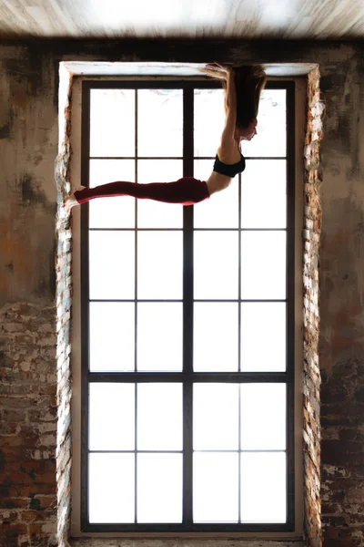 Menina Yoga em uma parte superior preta e leggings vermelhos está em suas mãos na janela de uma grande janela — Fotografia de Stock