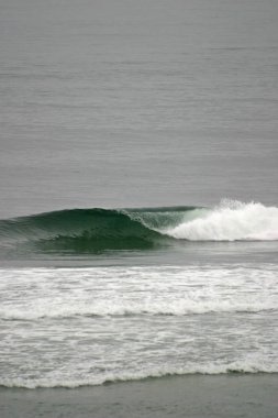 Sahilde kırılan dalgalar, sprey, beyaz su ve ışık suyun yüzeyine yansıyor..