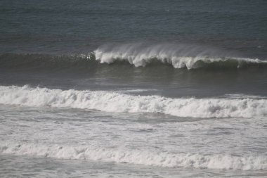Sahilde kırılan dalgalar, sprey, beyaz su ve ışık suyun yüzeyine yansıyor..