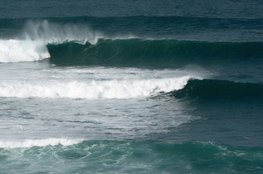 Sahilde kırılan dalgalar, sprey, beyaz su ve ışık suyun yüzeyine yansıyor..