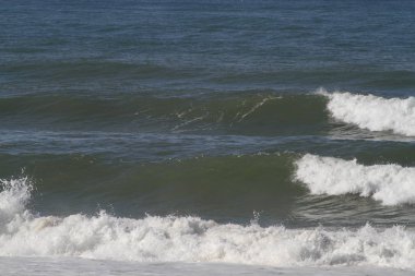 Sahilde kırılan dalgalar, sprey, beyaz su ve ışık suyun yüzeyine yansıyor..