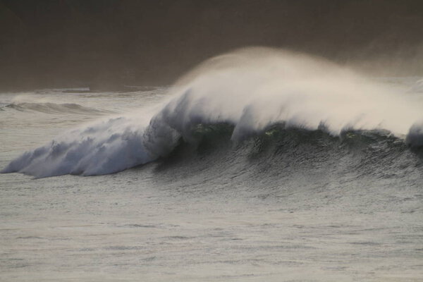 Волны разбиваются на побережье, брызги, белая вода и свет отражаются на поверхности воды.