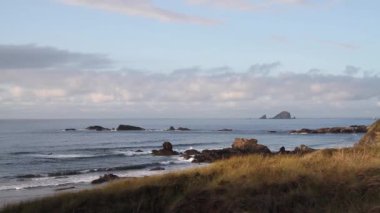 Deniz, dalgalar, bulutlu, mavi gökyüzü günbatımı sırasında ön planda çim taşları ile Atlas Okyanusu kıyısında