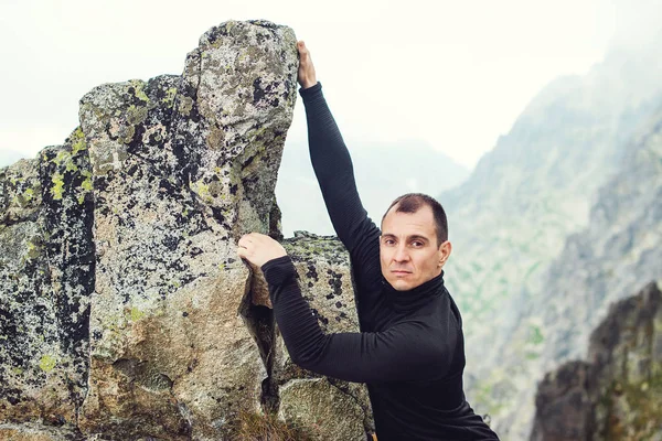 Young man climbs the rock against a mountain background.