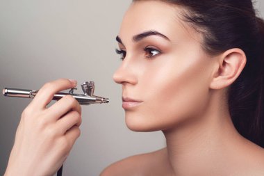 Airbrush ile telafi etmek. Kız yüz mükemmel deri ile. Çıplak makyaj ile manken. Makyaj dudaklar. Şehvetli kız. Airbrusher kullanarak makyaj sanatçısı. Gri izole.