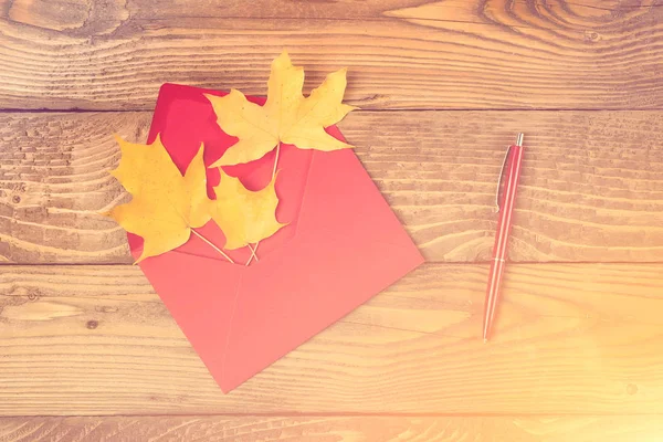 Red envelope with autumn leaves. Autumn letter. Maple leaves in red envelope, red pen on wooden background. Fall season. Autumn holidays concept. Autumn mood concept