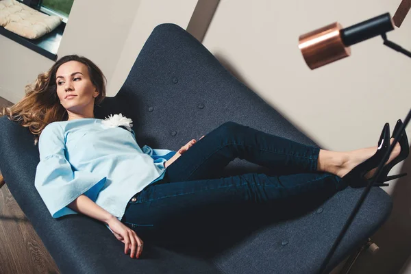 Stylish business woman taking a break. Attractive young woman lying on grey sofa in a modern office. Fashion girl resting on the couch in stylish shoes high heels. Fashion, beauty and lifestyle concept.