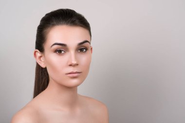 Esmer modeli gri arka plan, kopya alanı üzerinde çıplak makyajlı. Güzellik kız iri gözlü, çıplak omuz ile karanlık kaşları. Cilt ve kaş kavramı bakımı. Doğal deri kadın yüzü