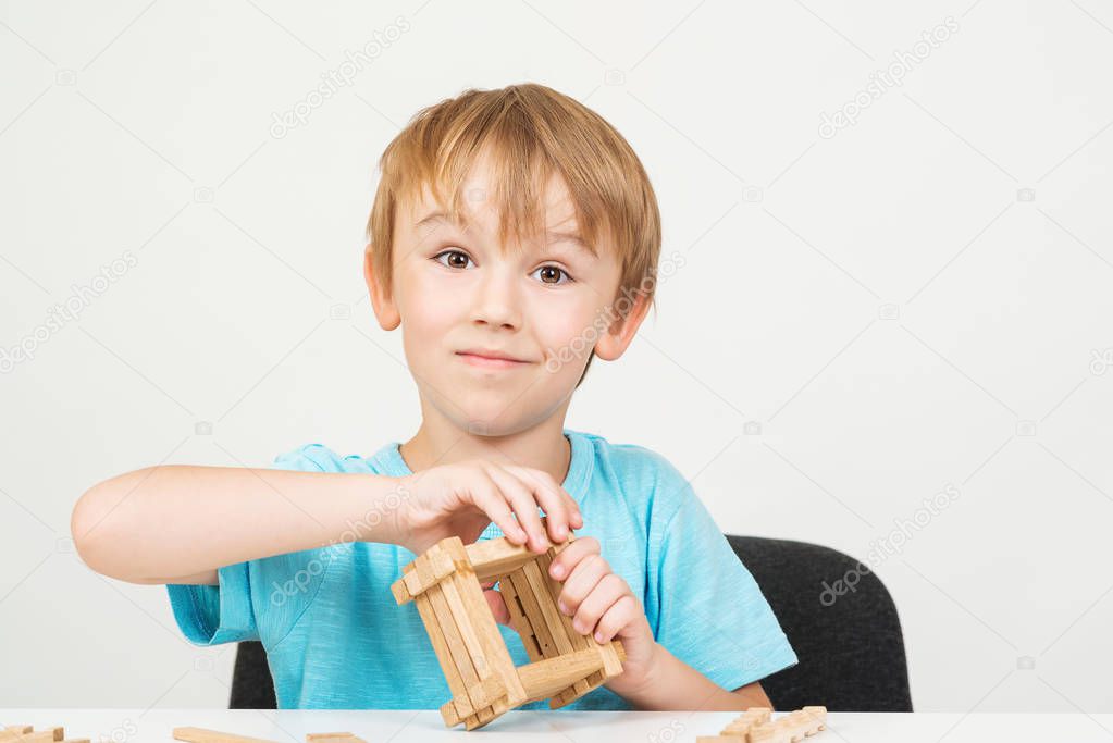 Cute boy playing with wooden blocks, isolated on white background. Education. Studio shot. Back to school concept. Happy childhood. Kid with happy or surprised face, building wooden structure
