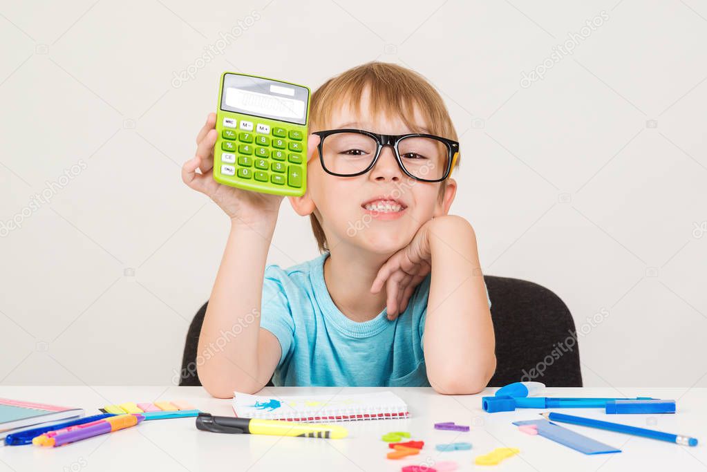 Smart boy using calculator. Kid in glasses figuring out math problem. Developing logical skills. Happy school boy doing homework. Smart kid in glasses at table with school supplies. Back to school