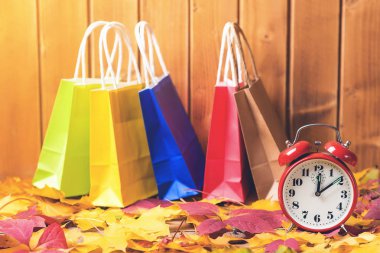Retro çalar saat ile düşen yapraklar arka plan üzerinde renkli alışveriş torbaları. Mevsimlik satış için zaman. Sonbahar konsepti alışveriş. Sonbahar satış. Kağıt torbalar alışveriş ile renkli sonbahar yaprakları