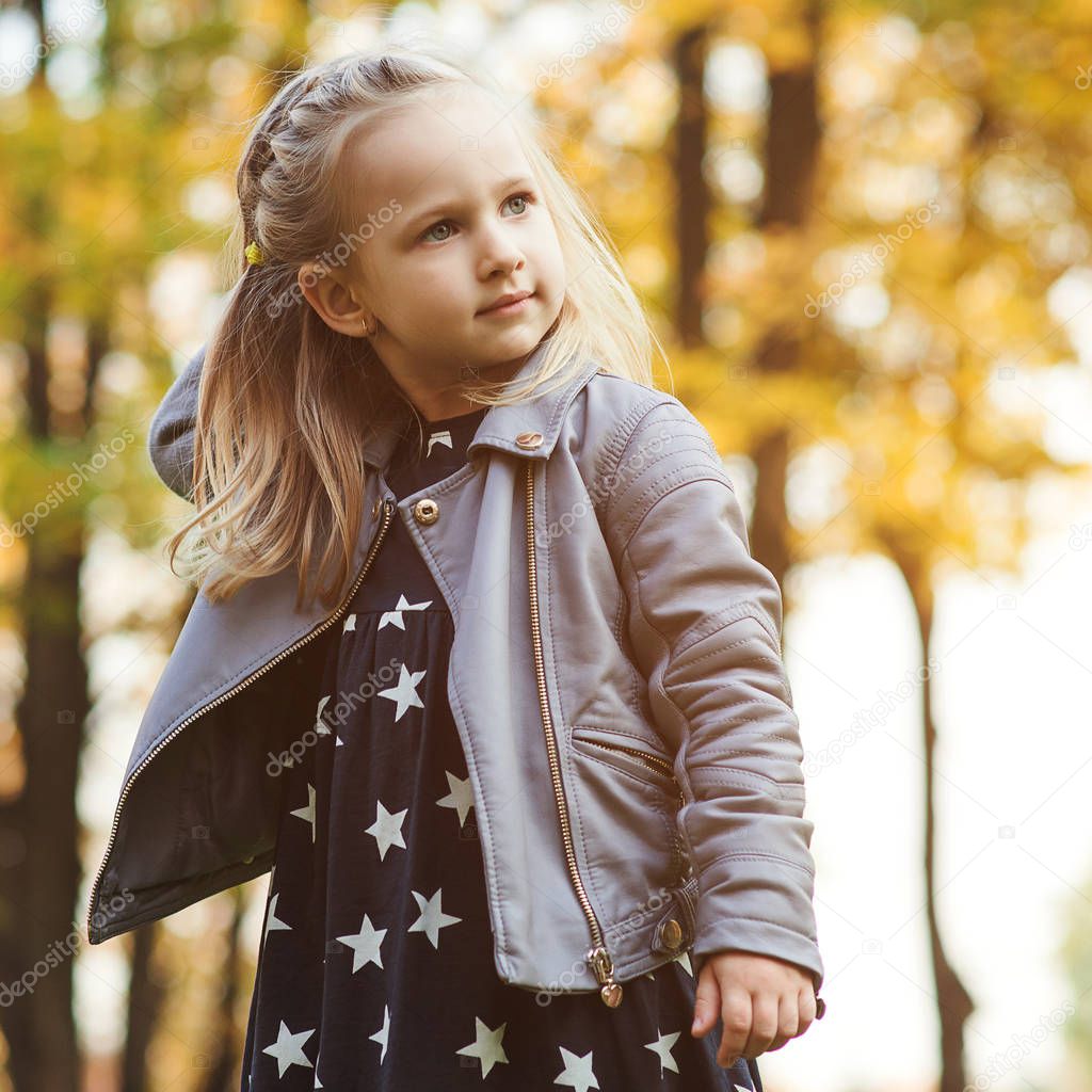 Autumn portrait of little girl in park. Little girl having fun in autumn. Happy childhood. Stylish girl playing in the city park. Autumn kids fashion. Seasonal sales