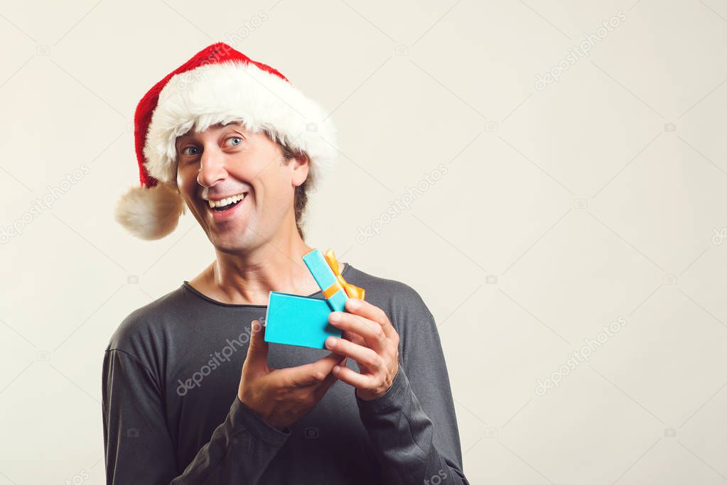 Surprised man opening Christmas gift over white. Handsome man in Santa hat with present, enjoying Christmas. Copy space. Christmas mood.