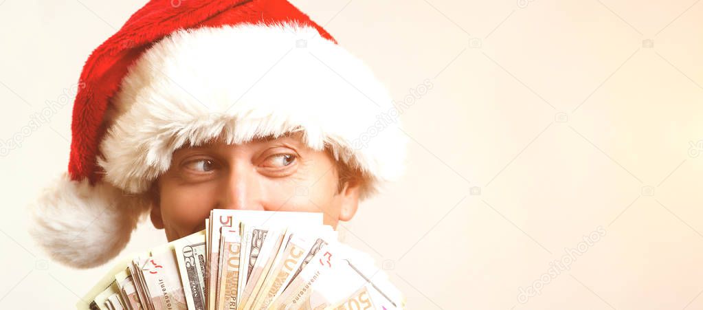 Young businessman in Christmas Hat covered his face with money over white background, copy space. Santa holding up fanned out handful of cash. Christmas, sale, banking, winning and holidays concept