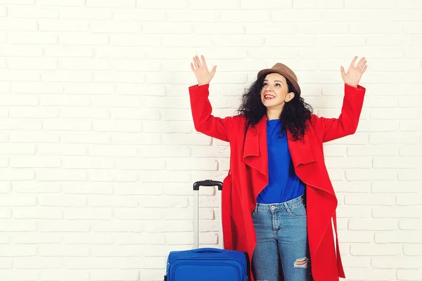 Surprising girl before traveling. Excited young caucasian woman dressed in red coat and hat with suitcase. Woman ready for trip, isolated on white. Copy space. People, travel and lifestyle concept