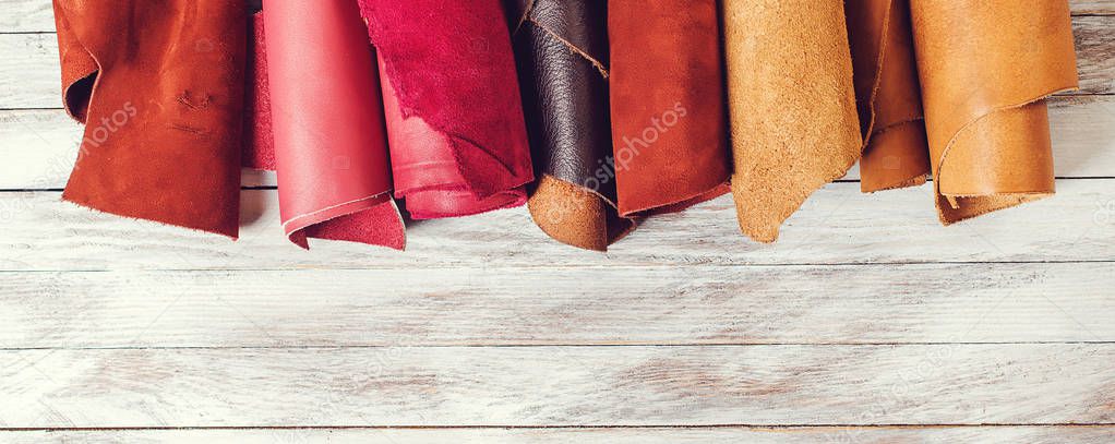 Rolls of natural color leather. Materials for leather craft. Copy space. Multi colored leather in rolls. Top view. Handmade craft. Different samples of leather on wooden table