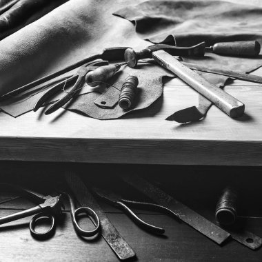 Eski araçları masada. Ayakkabıcı işyerinde deri parçaları. Shoemaker'ın çalışma masası. Deri el sanatları araçları ahşap arka plan üzerinde. Shoemaker araçları. Shoemaker'ın dükkanı. Siyah ve beyaz. Ayakkabıcı işçilik