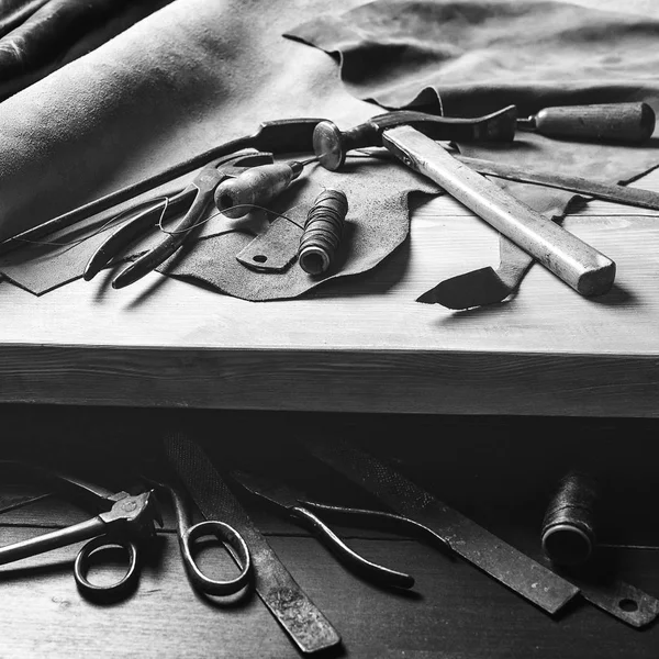 Old tools at table. Pieces of leather at cobbler workplace. Shoemaker's work desk. Leather craft tools on wooden background. Shoemaker tools. Shoemaker's shop. Black and white. Cobbler workmanship