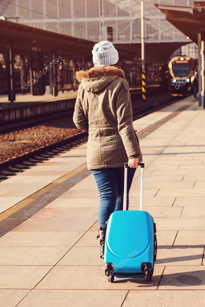 Young tourist woman walking, dragging luggage suitcase bag. Girl at railway station. Journey concept. Lifestyle, travelling, vacation. Autumn, winter travel. Woman in hat with suitcase back view