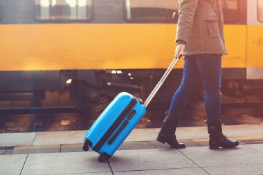 Tren istasyonunda yürüyen turist kadın. Tren. Kız sürükleyerek mavi bagaj bavul. Yolculuk kavramı. Yaşam biçimi, seyahat, tatil. Sonbahar, kış seyahat. Kadın mavi çanta