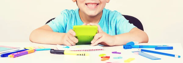 Boy with calculator doing homework at home. Child is sitting at a desk indoors. Back to school. People, children and education concept. Elementary school. Little student boy studying at school