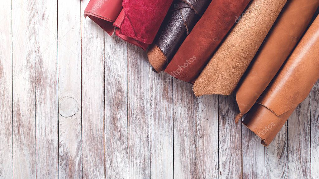 Multi colored leather in rolls. Flat lay. Rolls of natural color leather. Materials for leather craft. Copy space. Top view. Handmade craft. Different samples of leather on wooden table