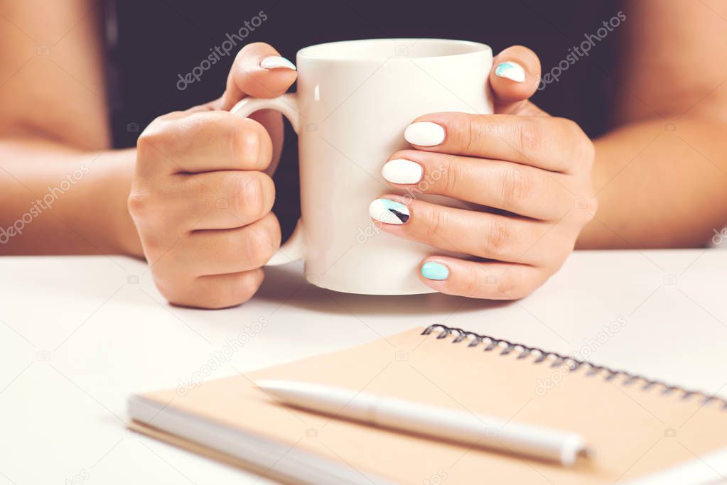Girl with beautiful manicure hold white cup in hand. Mockup for designs. Woman hand hold cup of tea. Female working desk