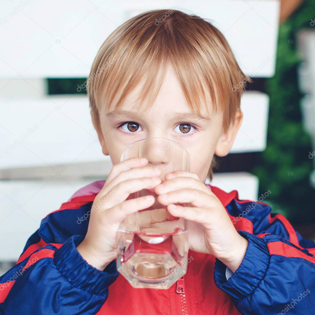 Cute little sporty boy drinks water. Kid outdoors. Child holds a glass of water. Kid with a glass of fresh water. Healthy and sporty childhood