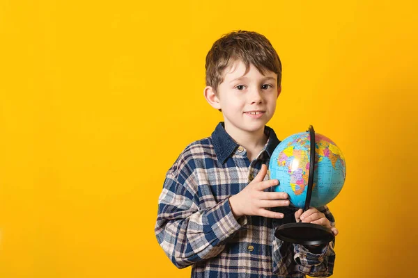 Funny kid with globe, isolated on yellow. Back to school concept. Educational globe. Curious child holding earth globe map in his hand. Little traveler, exploring new horizons at globe. Copy space.